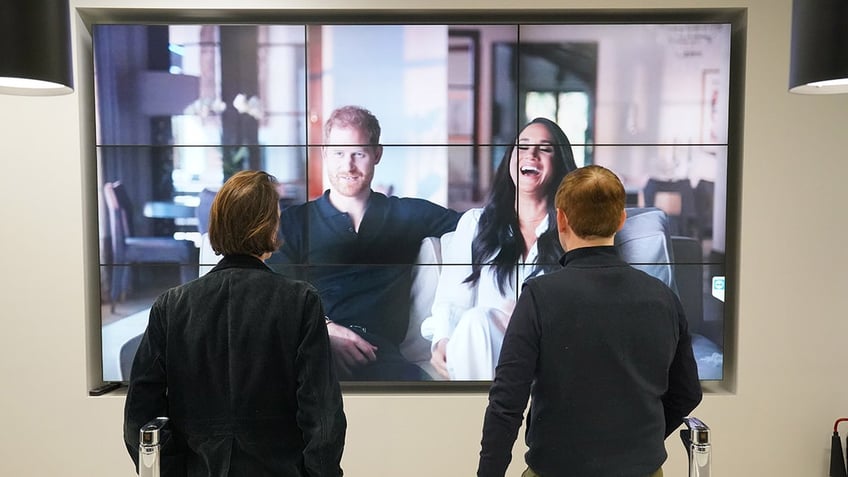 Two men watching Harry and Meghan on the big screen.