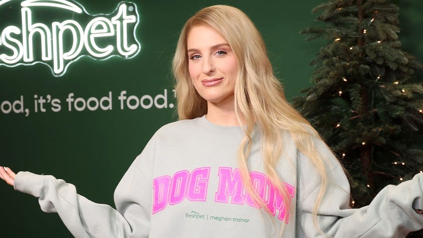 Meghan Trainor in a grey sweatshirt that says 'DOG MOM' in pink letters looks at the camera