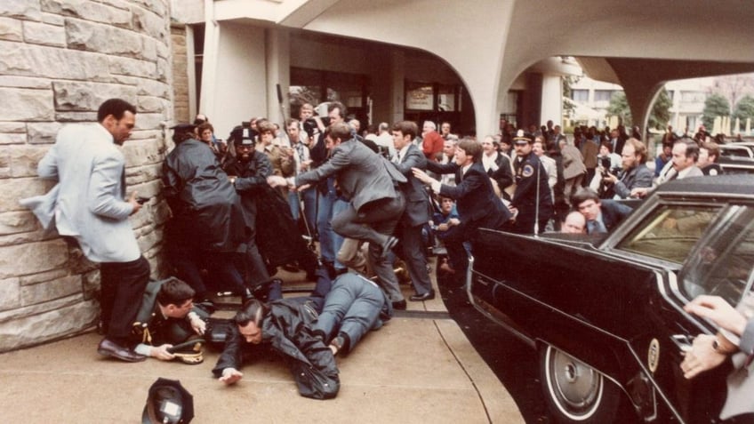 View of police officers and Secret Service agents as they dive to protect President Ronald Reagan amid a panicked crowd during an assassination attempt (by John Hinckley Jr) outside the Washington Hilton Hotel, Washington DC.