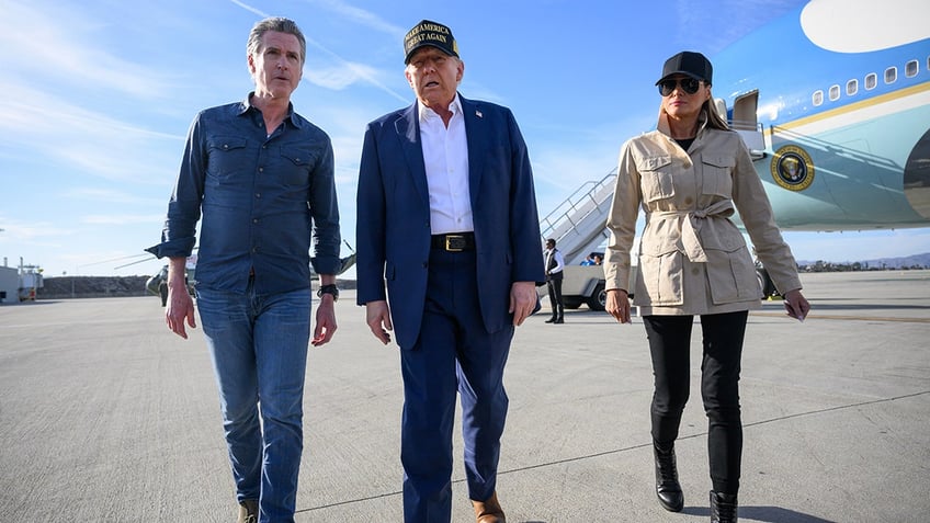 US President Donald Trump (C) approaches reporters to speak, flanked by First Lady Melania Trump (R) and California Governor Gavin Newsom, upon arrival arrival at Los Angeles International Airport in Los Angeles, California, on January 24, 2025, to visit the region devastated by the Palisades and Eaton fires.