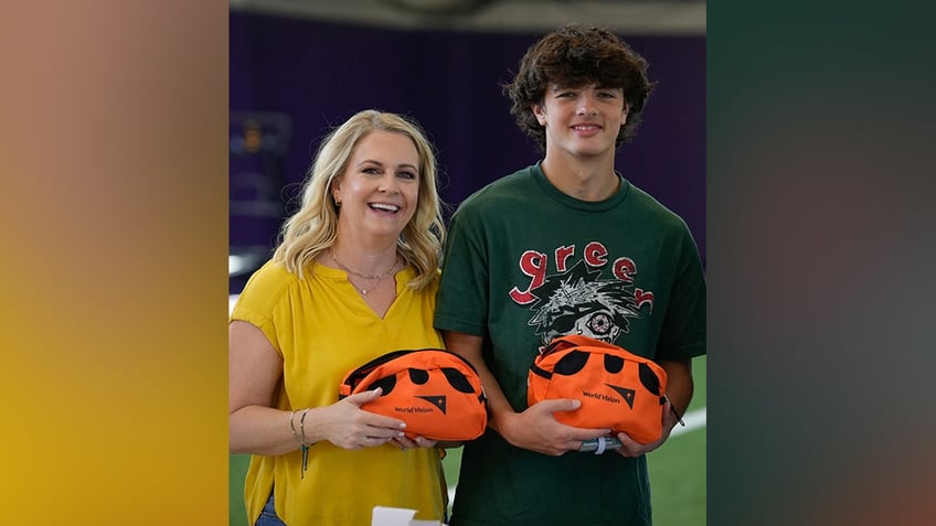 Melissa Joan Hart in a bright yellow shirt holds an orange hygiene bag for World Vision with her son in a green shirt, also holding a hygiene kit