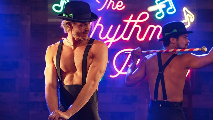 Chad Michael Murray in a black hat and black suspenders dances on stage in a still from "The Merry Gentlemen"