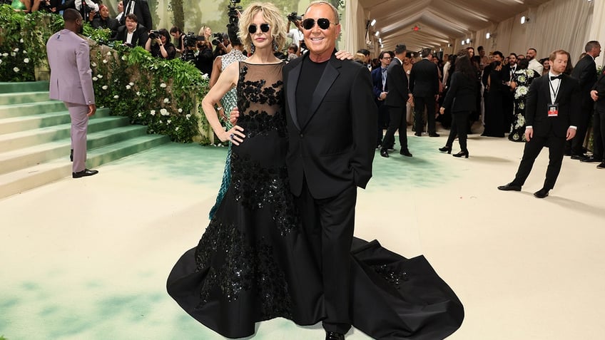 Meg Ryan at the Met Gala 2024 red carpet in a black Michael Kors dress walking with the designer