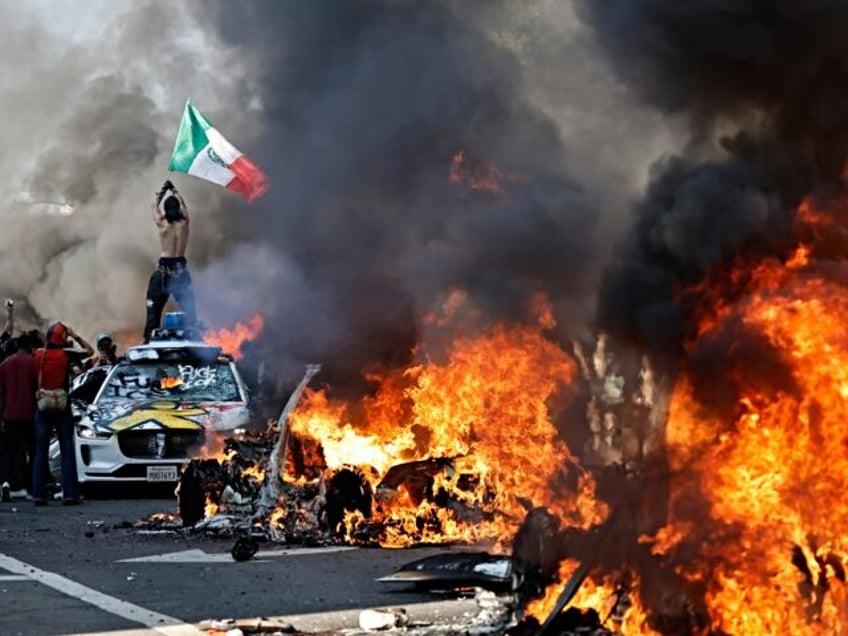 LOS ANGELES, LOS ANGELES - JUNE 08: A protestor holds up a Mexican flag as burning cars li