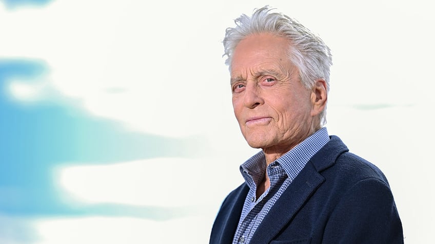 Michael Douglas in a navy suit and blue shirt looks out at the crowd at Cannes