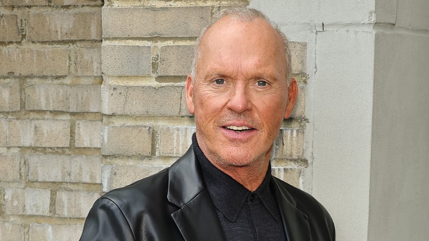 Michael Keaton outside in New York City wearing a black leather jacket smiles for the camera