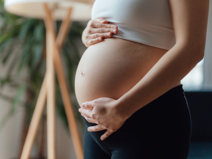 Side view close-up of pregnant woman touching her belly. Pregnancy health & wellbeing concept.