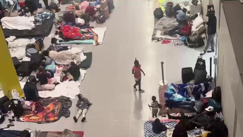 Migrants on both side of corridor on airport floor resting