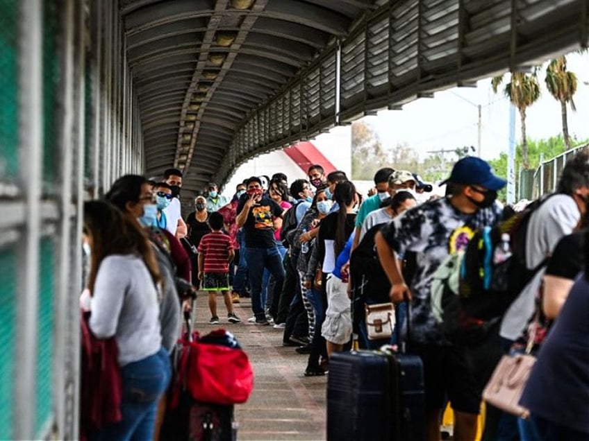 Migrants mostly form Central America wait in line to cross the border at the Gateway International Bridge into the US from Matamoros, Mexico to Brownsville, Texas, on March 15, 2021. - It's the new normal for migrant families under President Joe Biden, after the harsh "zero tolerance" approach of Donald Trump dashed the dreams of hundreds of thousands hoping to escape endemic poverty and violence in Central America. Biden's pledge of a more humane approach though has sparked a new rush to the border, threatening to become a huge political liability. Republicans are accusing him of opening the country's doors to illegal border-crossers and sparking a "crisis" on the US-Mexico frontier, marked in Texas by the meandering Rio Grande river. (Photo by CHANDAN KHANNA / AFP) (Photo by CHANDAN KHANNA/AFP via Getty Images)
