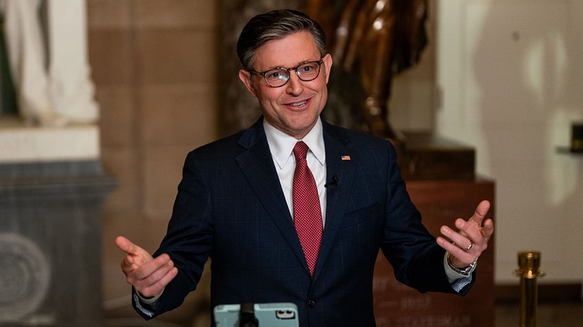 Speaker Mike Johnson smiling and holding his hands up near his sides as if to offer a point