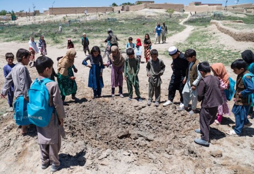 Children gather around a crater after Afghan deminers from the Halo Trust detonated an ant