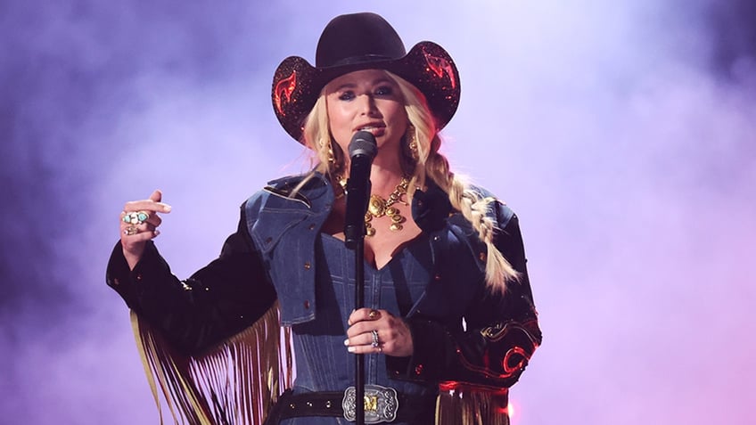 Miranda Lambert in a jean jacket with fringe points out while performing on stage