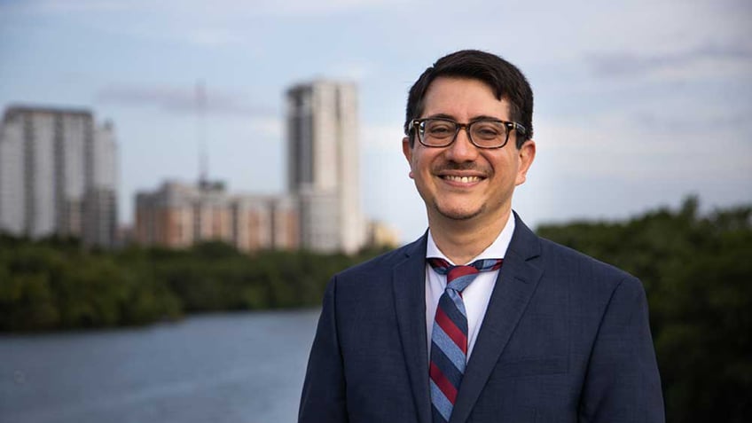 Jose Garza wearing a suit smiling in front of Austin skyline