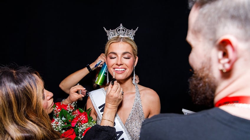 A makeup artist applying liquid lipstick to Miss America 2025 Abbie Stockard.