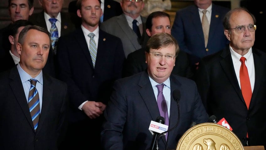 Mississippi Republican Gov. Tate Reeves, center, Jason White, left, and Republican Lt. Gov. Delbert Hosemann, right, with legislators behind them