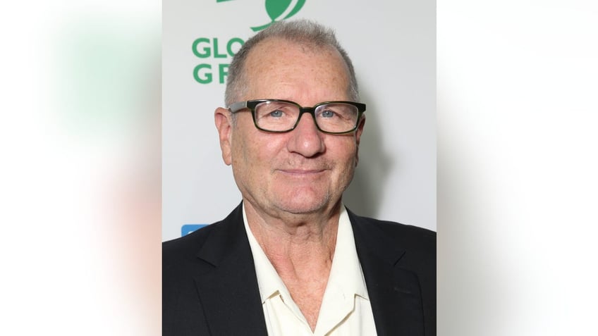 Ed O'Neill in a white shirt and black suit with dark frame glasses