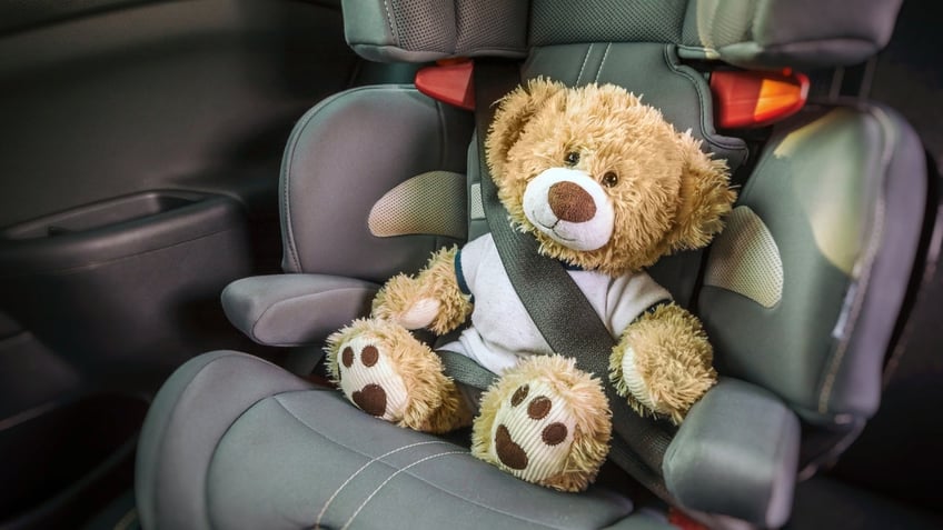 A teddy bear strapped into a carseat