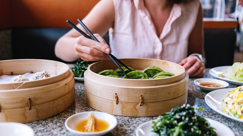 Woman eating dumplings and other Asian foods with chopsticks.