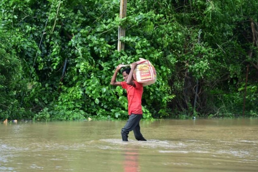 A man carries his belongings through a flooded street after heavy rains on the outskirts o