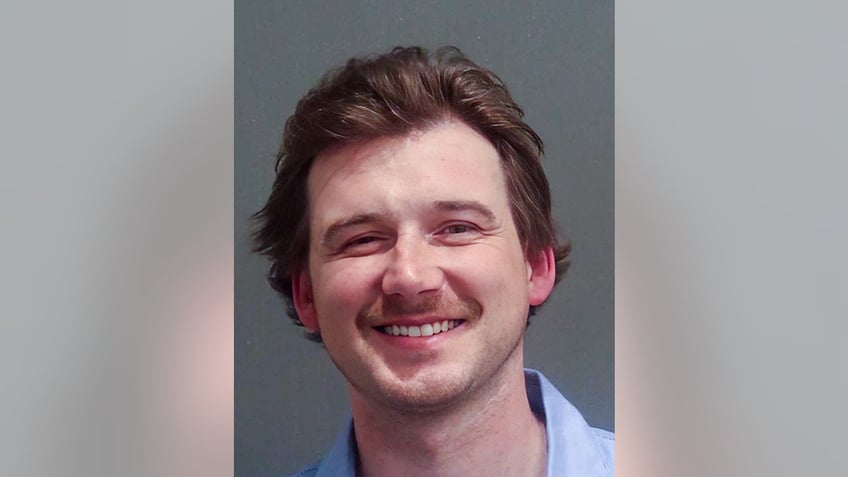 Morgan Wallen smiling in 2024 mugshot in blue button-down shirt