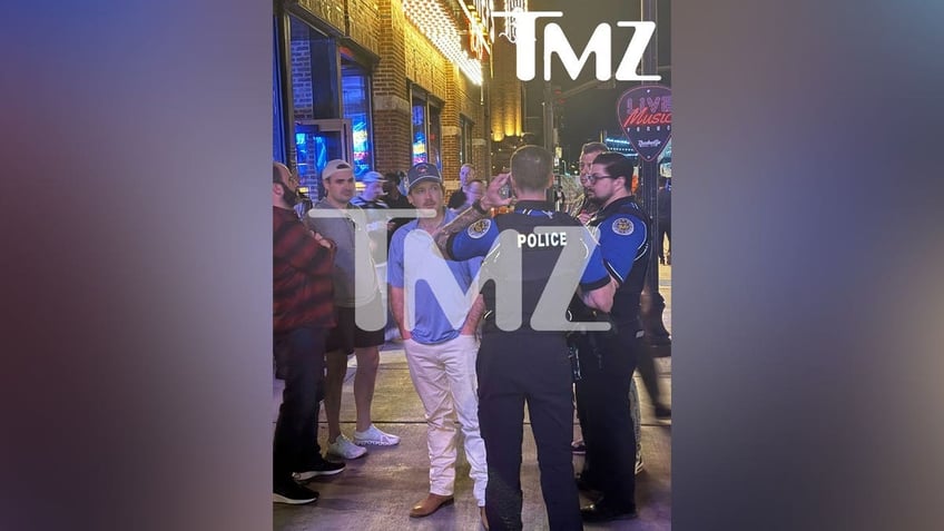 Morgan Wallen wears white slacks and a blue shirt while talking to police officers after throwing chair off roof