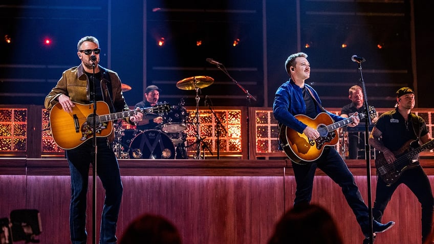 Morgan Wallen and Eric Church strum guitars on stage at awards show in Nashville.