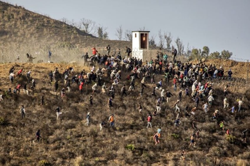 Migrants storm a barbed-wire fence as they attempt to cross the land border with Spain's A