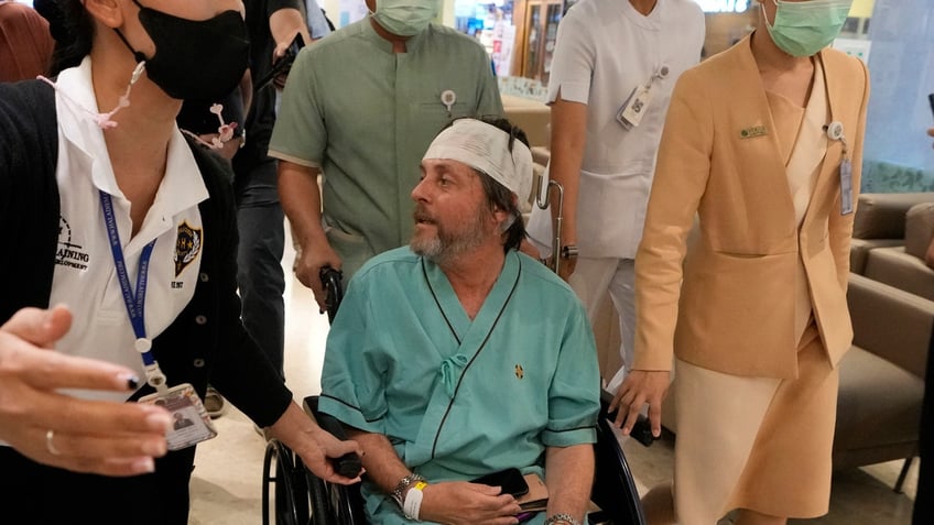 An Australian passenger, center, who was injured on a flight that was battered by severe turbulence, talks to reporters at Samitivej Srinakarin Hospital in Bangkok, Thailand.