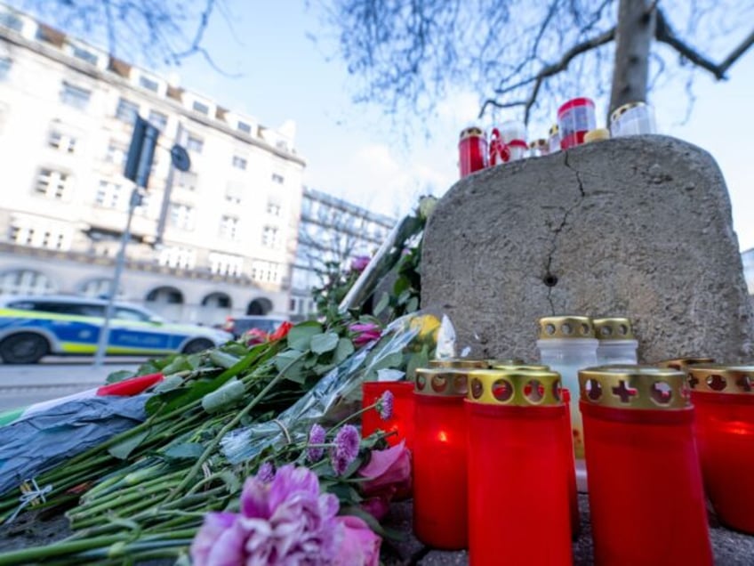 15 February 2025, Bavaria, Munich: A police emergency vehicle drives past flowers and cand