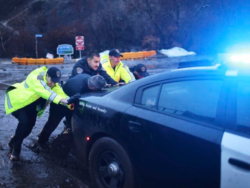 Police officers push an emergency vehicle stuck in mud in the Palisades Fire zone during a