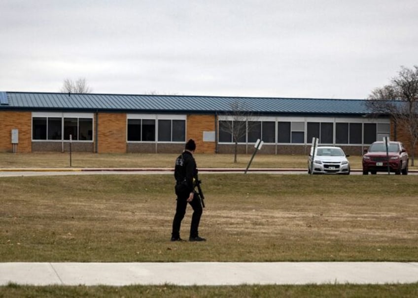 An armed police officer walks the perimeter of the Perry High School in Iowa after a shooting