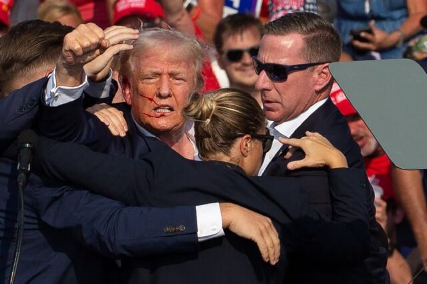 Donald Trump is seen with blood on his face surrounded by Secret Service agents as he is t