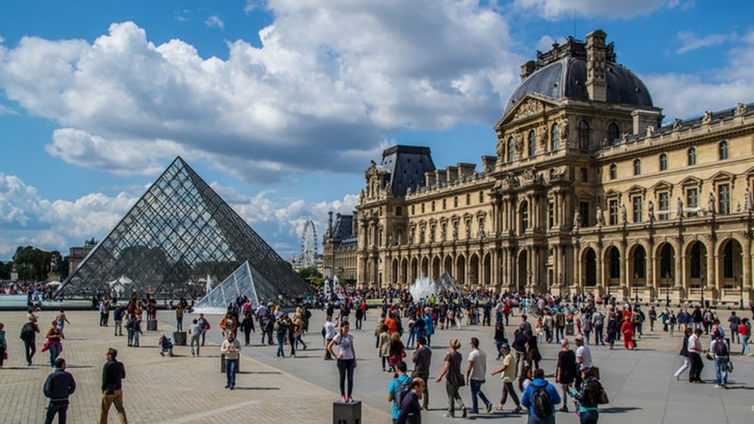 Paris, France - August 15, 2014: Beautiful picture of the Louvre Museum located in Paris, France. The picture shows the pyramid entrance and the main building at the right side. Some people walking around and taking photos can also be seen in the picture.