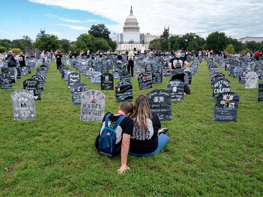 People who lost relatives to a drug overdose sit among imitation graves set up by the Trai