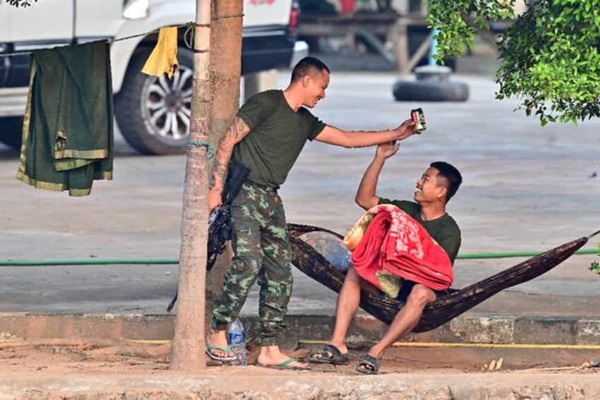 A member of a Myanmar militia holds a beer can and a weapon while talking to a comrade acr