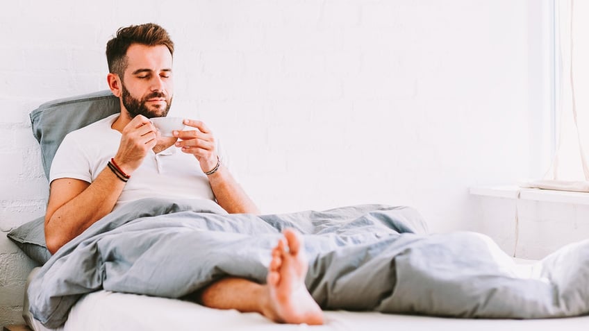 Young man drinking coffee in bed