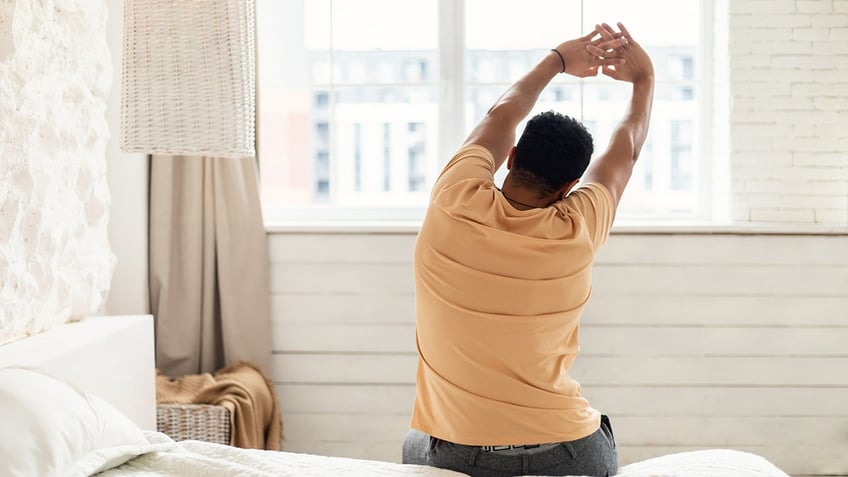 Man Sitting On Bed Stretching Arms