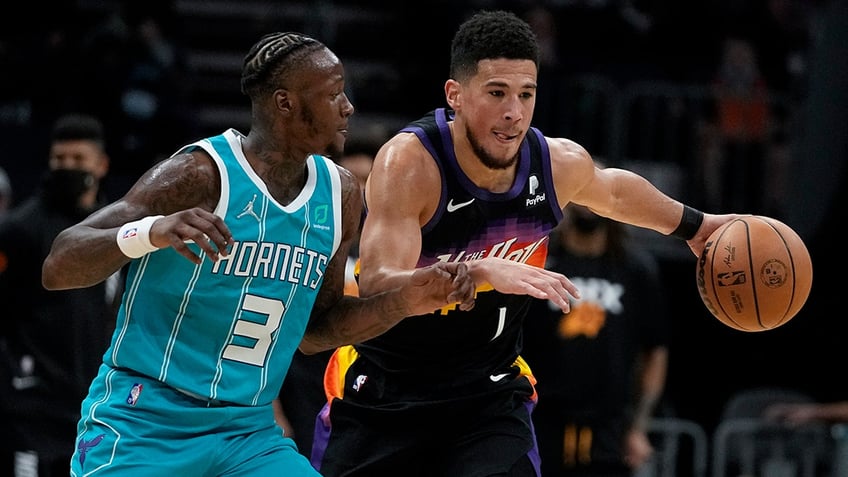 Phoenix Suns guard Devin Booker drives to the basket past Charlotte Hornets guard Terry Rozier during the first half of an NBA basketball game on Sunday, Jan. 2, 2022, in Charlotte, N.C.