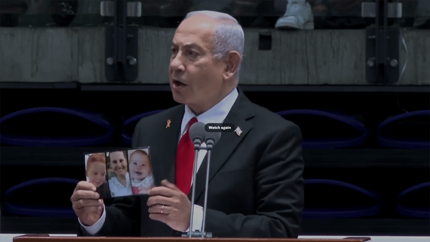 Netanyahu at the podium holding up Bibas family photo