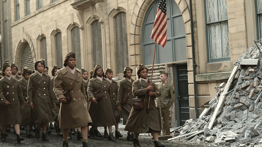 The 6888th postal battalion marches down a street in a scene from Netflix's "The Six Triple Eight." A woman in the lead holds up an American flag.