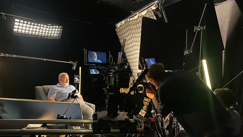 A side-view of Ed Parze sitting in front of a camera crew.