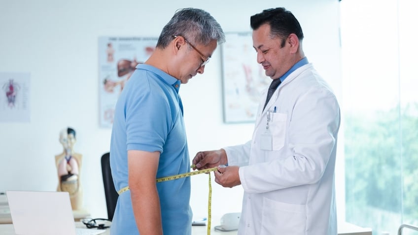 Doctor measuring man's waist