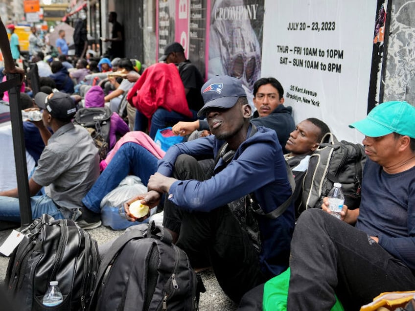 Migrants sit in a queue outside of The Roosevelt Hotel that is being used by the city as t