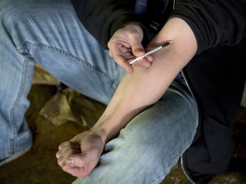 In this June 13, 2017, file photo, a man injects heroin into this arm under a bridge along