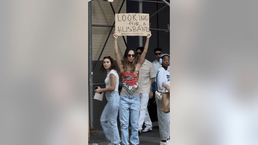 new york woman walks down the street with a looking for a husband sign sparking plenty of conversation