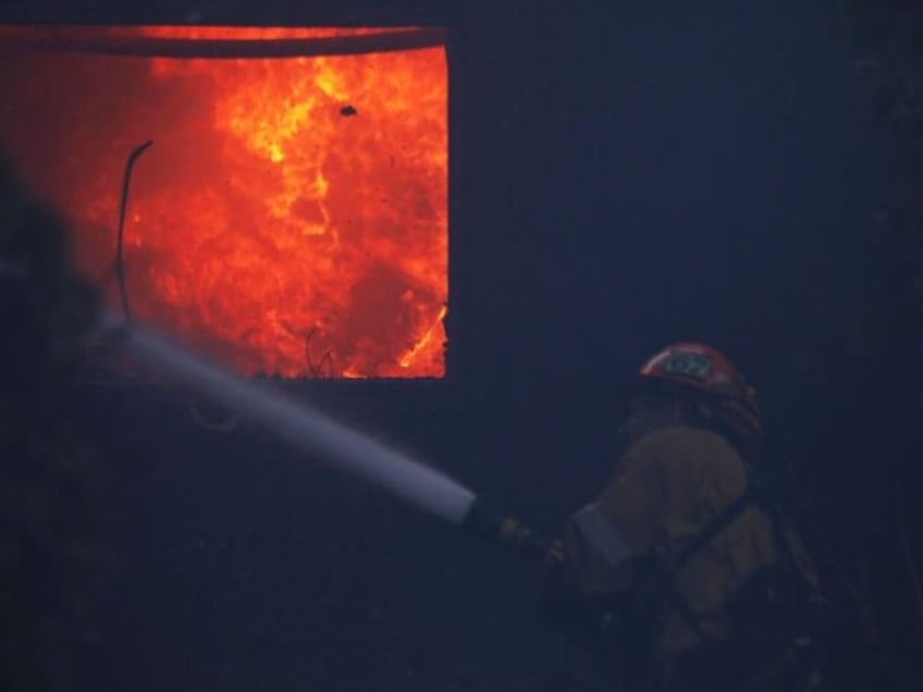 A firefighter works to put out a brush fire burning near homes in Pacific Palisades, Calif