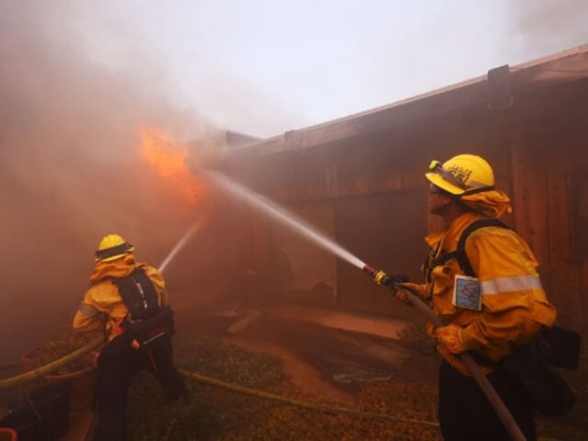 Firefighters work to extinguish flames engulfing a home as a brush fire rages in Pacific P