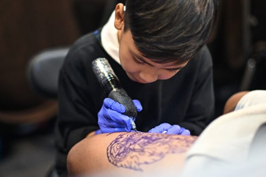 Wielding a cumbersome tattoo gun, nine-year-old Napat Mitmakorn inks the pattern of a fang