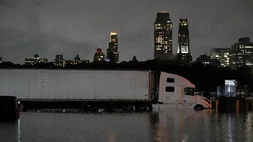A semi-truck submerged in water in front of buildings