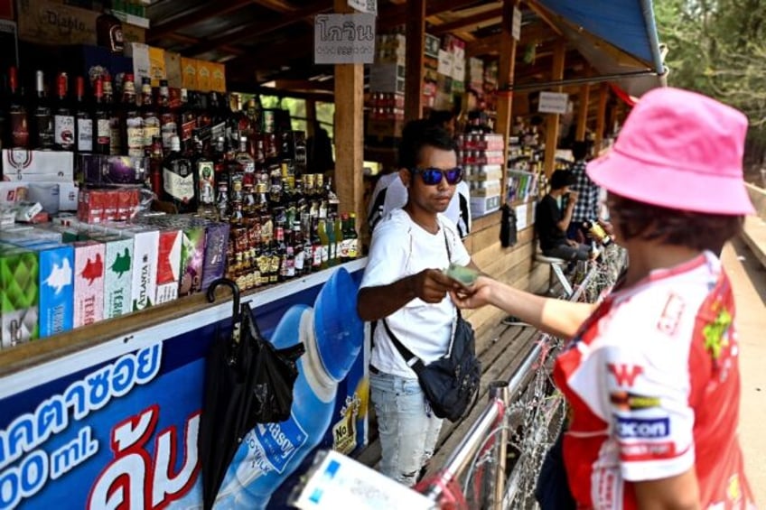 A Myanmar vendor sells alcohol and cigarettes over a barbed-wire fence in "no-man's land"